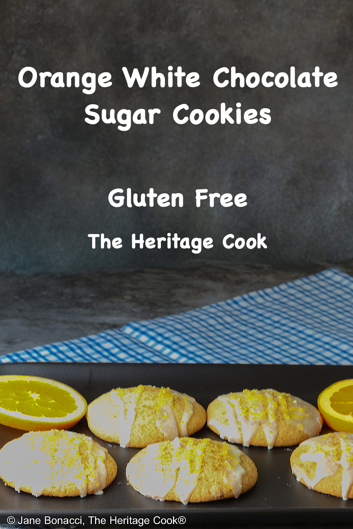 5 Large Orange and White Chocolate Sugar Cookies with two orange slices on a black rectangular platter with a blue checked cloth behind, each cookie drizzled with white chocolate glaze and sprinkled with yellow sparkling sugar © 2026 Jane Bonacci, The Heritage Cook.