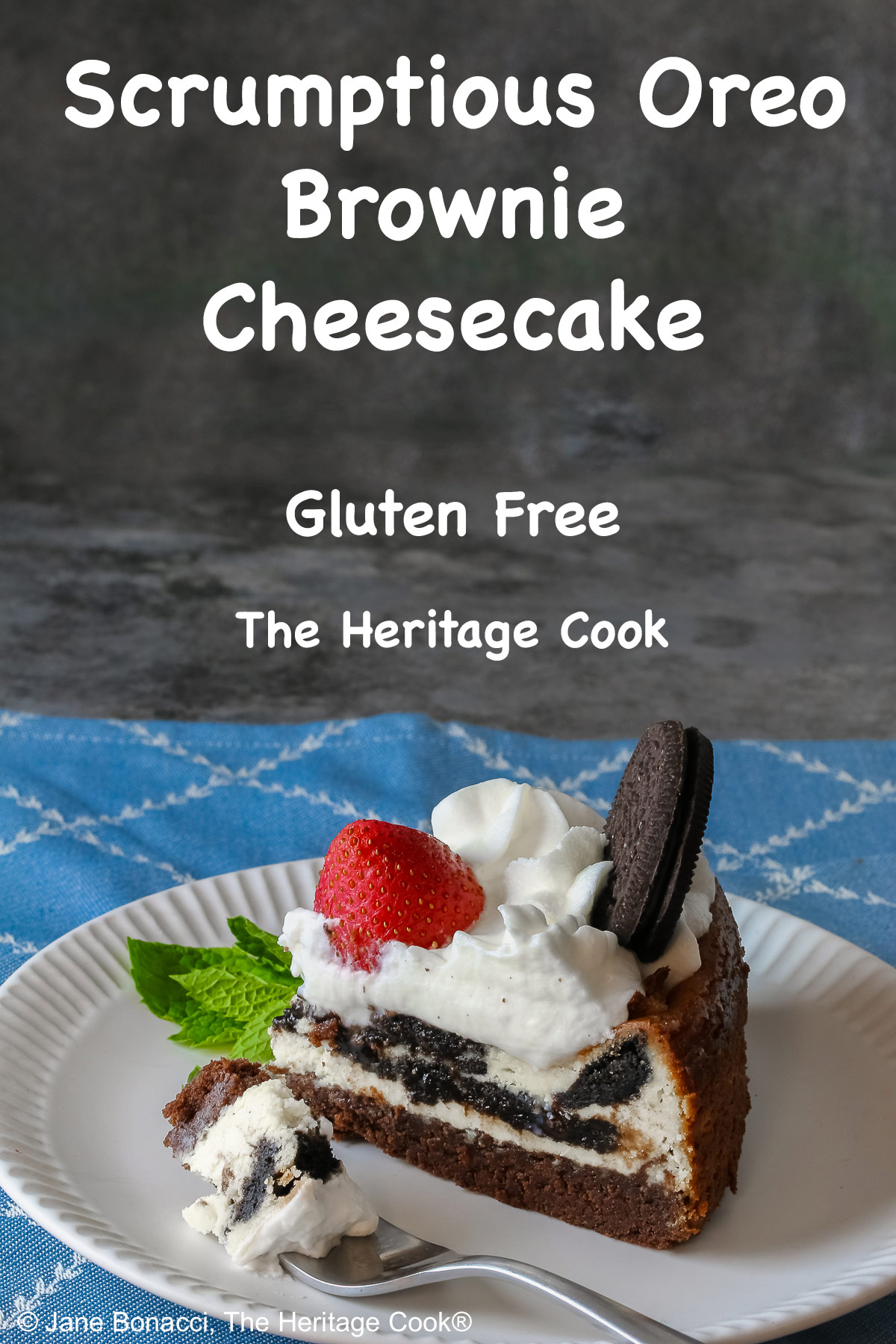 A slice of Scrumptious Oreo Brownie Cheesecake, topped with freshly made whipped cream, a whole Oreo cookie, and a whole strawberry, with a sprig of mint alongside © 2026 Jane Bonacci, The Heritage Cook.