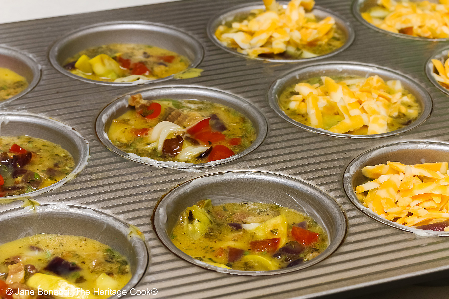 Muffin tins filled with the egg/vegetable mixture being topped with cheeses.
