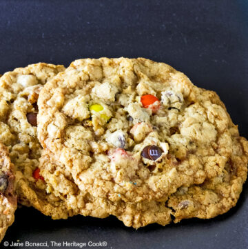 Close up of a loaded cowboy cookie leaning on another cookie with a black background.