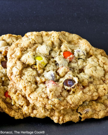 Close up of a loaded cowboy cookie leaning on another cookie with a black background.
