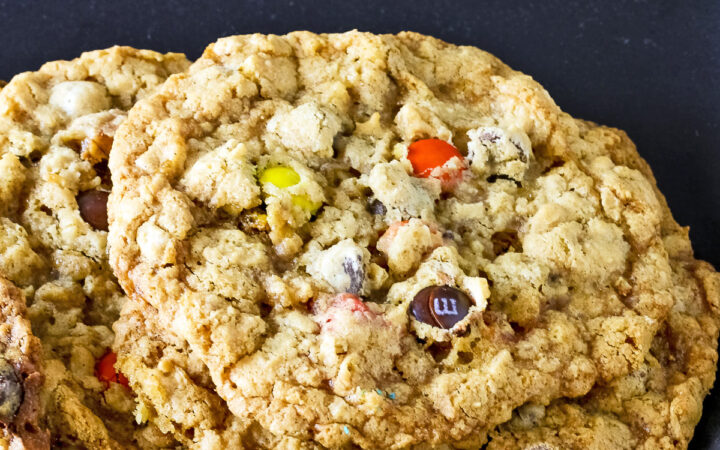 Close up of a loaded cowboy cookie leaning on another cookie with a black background.