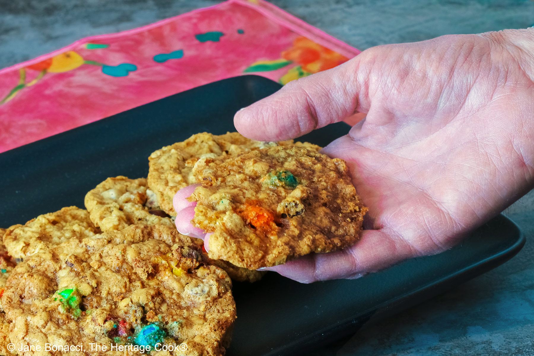 Hand holding a cookie, suspended above the tray of cookies.